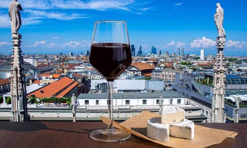 Glass of red wine with brie cheese against view from above of Milan, Italy