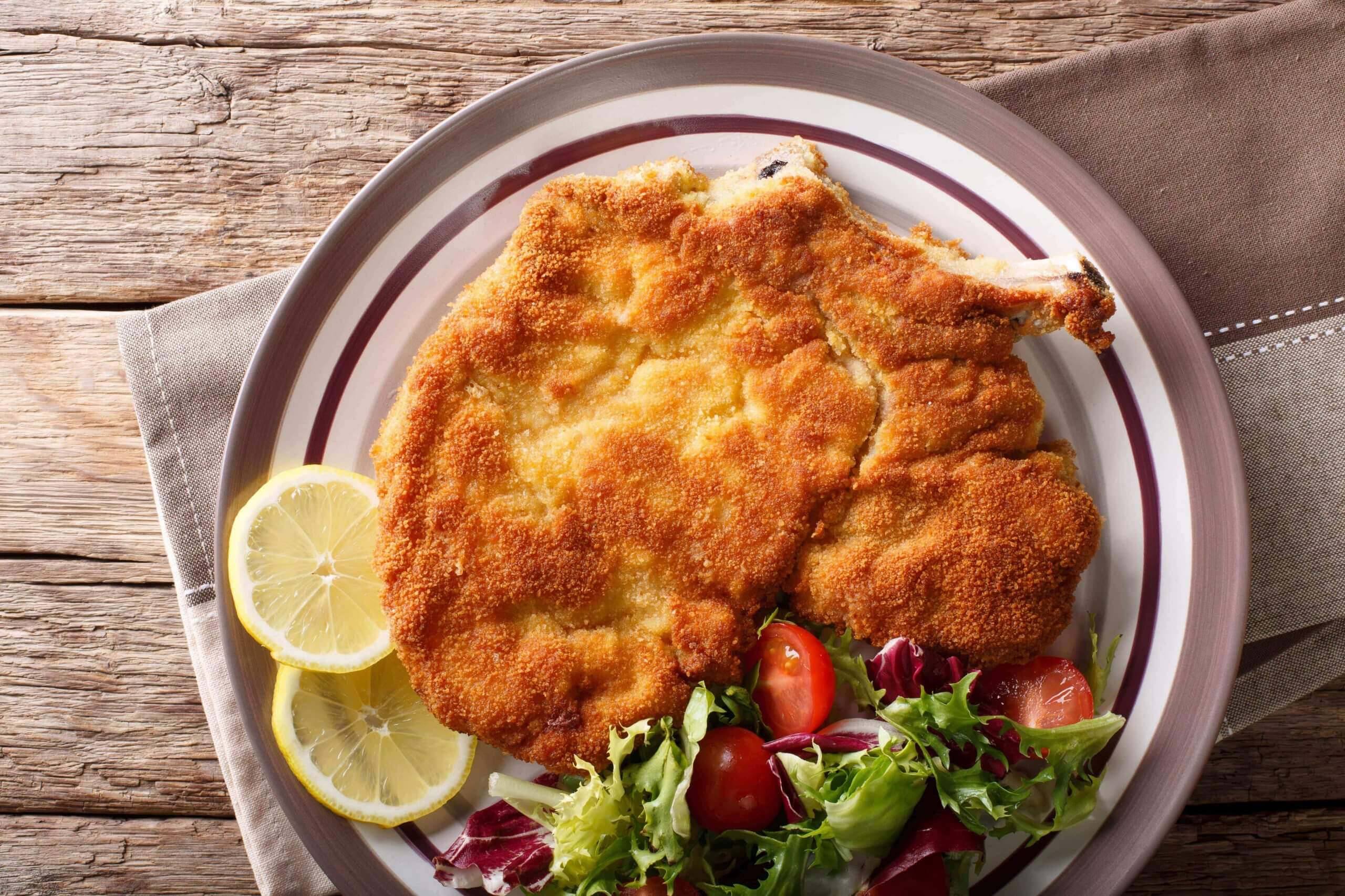 A plate with traditional milan breaded chicken with lemons and salad