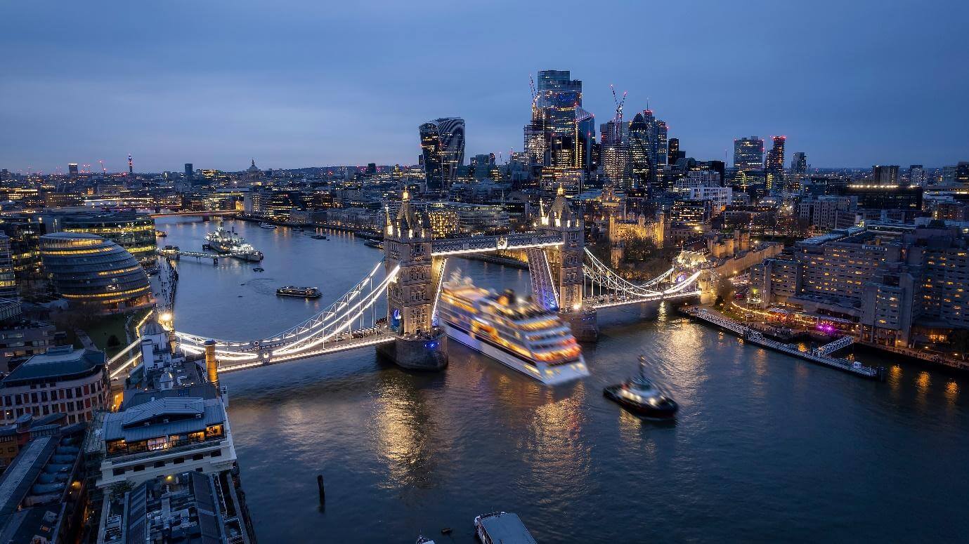 Aerial view of the skyline of London with a motion blurred cruise ship passing under the lifted Tower Bridge during dusk, England